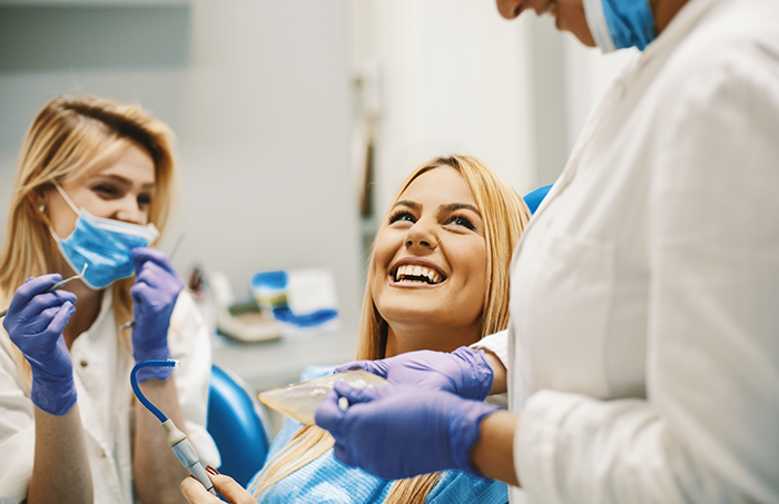 Dental patient smiling and looking up at two dentists in Fort Smith