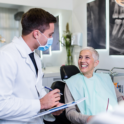 Dentist with clipboard talking to senior dental patient