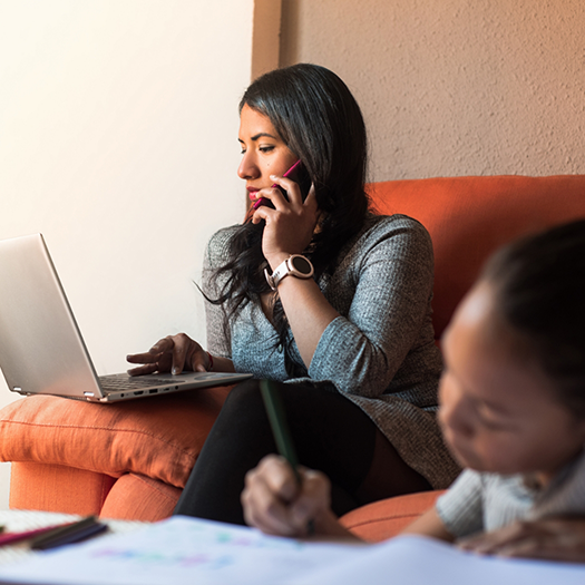 Woman on orange sofa talking on phone and working on laptop