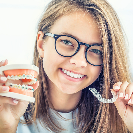 Woman with glasses holding clear aligners and model teeth with braces