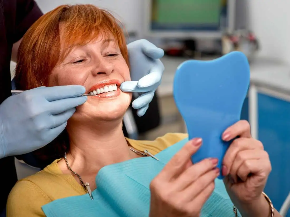 Female dental patient with red hair looking in handheld mirror