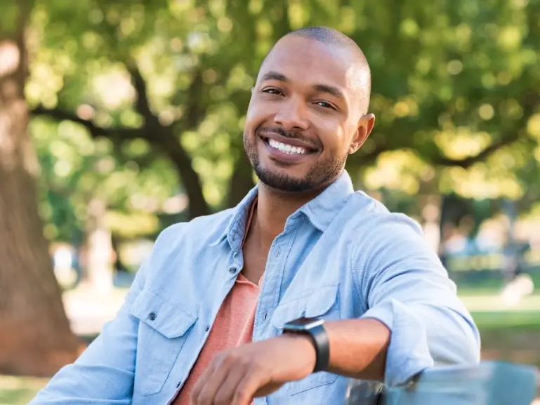 Man with blue jacket leaning on fence outside and smiling