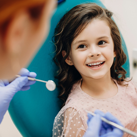 Little girl looking up at dentist holding dental instruments