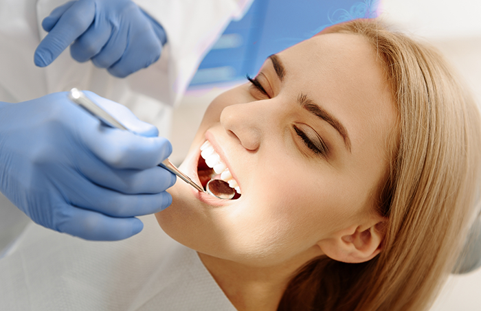 Female patient smiling while dentist examines teeth with mirror