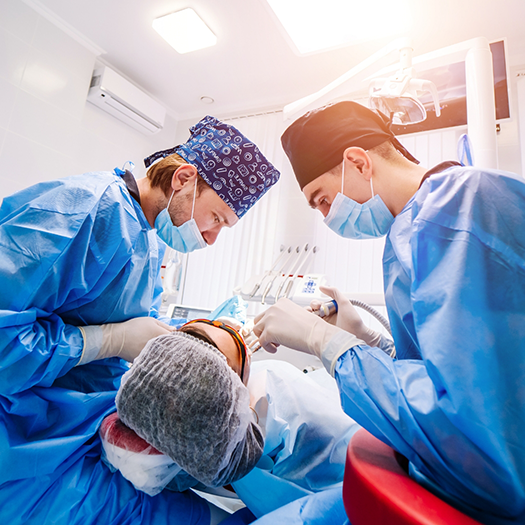 Two dentists with masks standing over a patient